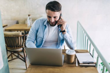 Gündelik giyinen, kafede çalışan, laptopçu bilgisayarı ve cep telefonu kullanan 20 'li yaşlarda zengin bir adam, akıllı telefon konuşmalarıyla online rezervasyon yaptığını onaylıyor.