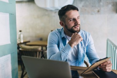Kafede serbest çalışan yaratıcı erkek girişimci dizüstü bilgisayarla iş kurma fikirleri üzerine kafa yoruyor planlayıcısı olan düşünceli hippi adam serbest çalışmaya odaklanıyor.