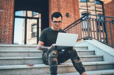 Laptop bilgisayarında çalışan yakışıklı grafik tasarımcısı dışarıda oturan 4G internete bağlı, erkek öğrenci sosyal ağlarda modern netbook aygıtıyla sohbet ediyor.