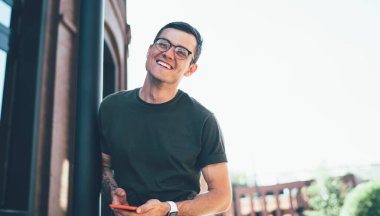 Şehir sokağındaki kameraya bakarken şık giyinen ve gözlük takan neşeli genç erkek yürüyüşçüden.