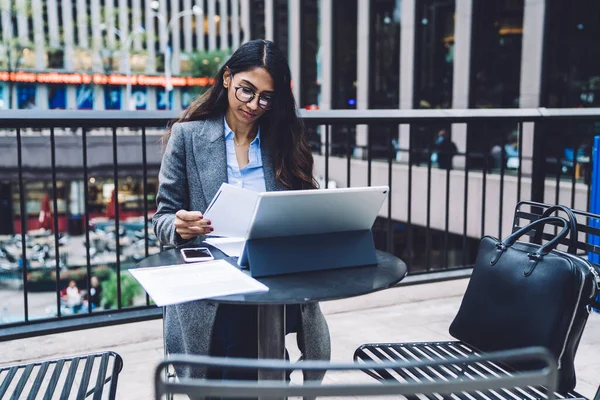 Çantası terasta oturan ve tablet, New York City 'de çalışırken gazete okuyan kendinden emin, genç bir etnik kadın.