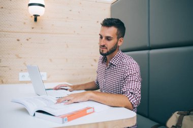 Gündelik giysiler içinde konsantre olmuş etnik öğrenci, kitap okuyor. Laptop kullanarak bilgi arıyor. Kafedeki masada oturmuş üniversite projesi yaratıyor.
