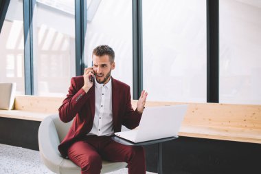 Resmi takım elbiseli kızgın adam, modern çalışma alanındaki masada oturan akıllı telefon hareketleriyle ilgili iş arkadaşı sorununu tartışıyor.