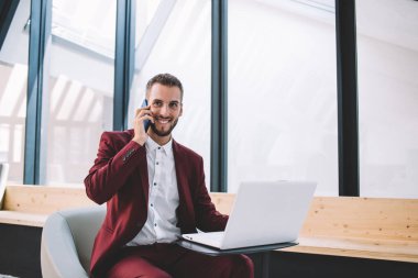 Resmi takım elbiseli neşeli etnik erkek, modern ofisteki partnerle iletişim kurmak için dizüstü bilgisayar kullanıyor.