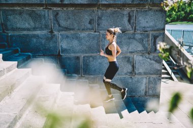 Güneşli bir günde açık hava stadyumunda koşarken şık giyinen kör saçlı genç bir kadının yukarıdan görünüşü ısınıyor. 