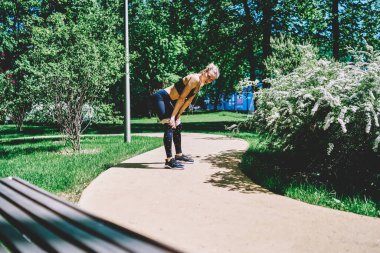 Siyah giyinmiş sıska sporcu kadın ve tozluklar yazın yeşil ağaçlar ve çalılarla parkta egzersiz yapıyor.