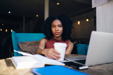 Kıvırcık saçlı, laptopta sörf yapan, kahve içen kahve içen, kafede kalemle dolu bir kadın.