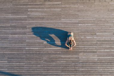 Spor kıyafetleri içinde tanınmayan bir bayanın ahşap zeminde yoga yapması ve kollarını bacaklarına uzattığında esneklik göstermesi.