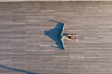 Spor giyimli, formda ve aktif bir kadının tahta zeminde sicim üzerinde oturması ve sabah antrenmanlarında esneme hareketleri.