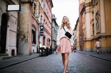 Düşünceli, çekici, modern, etekli, kemerli, sarışın bir kadın. Elinde cep telefonu olan bir dilenci. Yaşlı şehrin caddesinde yürüyor. 