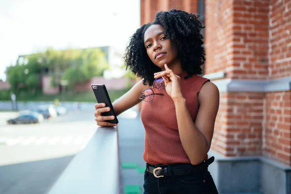 Молода Горда Чорна Жінка Тримає Мобільний Телефон Окуляри Стоячи Над — стокове фото