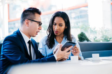 Düşük açılı, düşünceli, çok ırklı, iyi giyimli, ekrana odaklanan ve dijital tabletle etkileşime giren iş arkadaşları masada oturup, modern kafede kahve içerken,