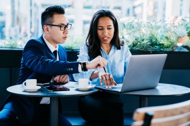 Zarif giysiler içinde, masaya oturup, kahve molası sırasında dizüstü bilgisayarla etkileşim kurarak sorunu çözmeye çalışan sorunlu meslektaşların düşük açılı görüntüsü.