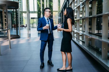 Yetişkin iş arkadaşları, şık kıyafetler içinde, sıcak bir içecekle birbirlerine bakıp sohbet ederken çağdaş gökdelenlerin lobisinde oturuyorlardı.