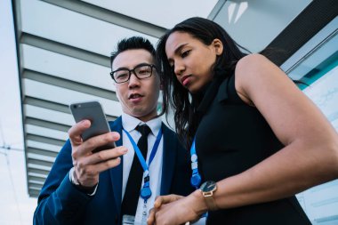 Kadın meslektaşımla cam koridorda durup mesajları okurken cep telefonunun ekranına bakarken gülümseyen Asyalı işçinin alçak açısı.