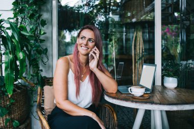 Kendine güveni tam, uzun saçlı, stil sahibi bir kadın. Akıllı telefondan sohbete katılıyor. Birlikte bakarken iş için yeşil kafedeki masada dizüstü bilgisayarında oturuyor.