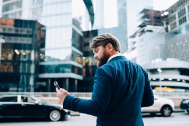 Modern şık takım elbiseli işadamının arka planı, şehir caddesinde trafiğe karşı akıllı telefon kullanıyor, arabaları ve modern binaları var. 