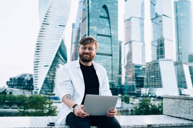 Pozitif yazılım geliştiricisinin portresi dizüstü bilgisayarla oturuyor ve kameraya gülümserken teknoloji güncellemesini bekliyor, günlük giyim ve gözlük takan mutlu bir öğrenci.