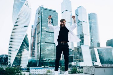 Yeni megalopolis keşfi için şık giyinmiş mutlu erkek turistin tam boy portresi. Başarılı beyaz gezgin elini kaldırıyor ve seviniyor.