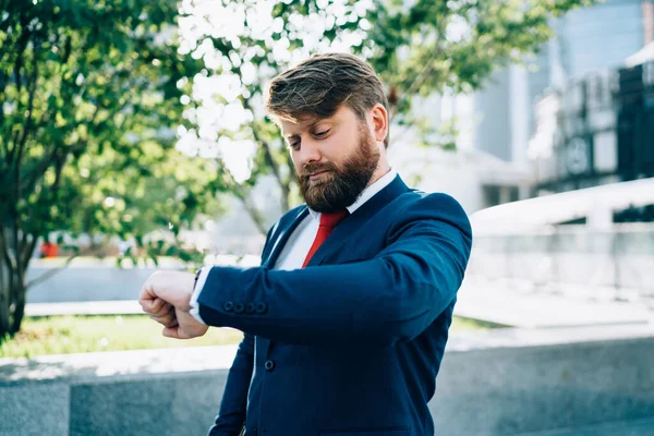 Ofis binasının önünde kırmızı kravatlı, takım elbiseli başarılı bir işadamı müşteriyle buluşmadan önce kol saatine bakıyor.