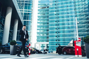 Resmi takım elbiseli başarılı genç adam, yaya geçidinde yürüme projesinin iş arkadaşı planıyla tartışmak için akıllı telefonu kullanıyor.