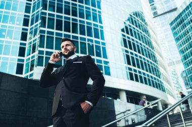 Takım elbiseli ciddi ve düşünceli bir adam merdivenlerde dikilirken telefonla konuşuyor.