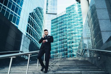 Meşgul yöneticilerin telefonda konuştuğu düşük açı ve büyük şehrin merdivenlerinden inerken kol saatini kontrol etmek.