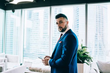 Resmi kıyafetler içinde başarılı bir erkek sosyal medyayı kontrol etmek için cep telefonu kullanıyor. Kafedeki kameraya bakarak işten rahatlıyor.