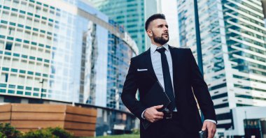 Şehir merkezindeki modern ofis binalarının karşısında duran siyah takım elbiseli başarılı ve odaklanmış bir adamdan.