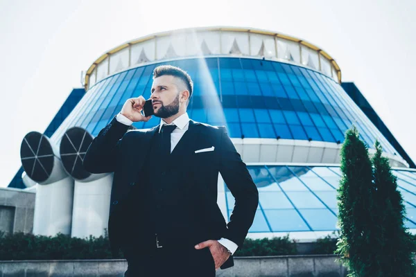 忙しいひげを生やした上品な男性で黒のスーツで話す携帯電話のスタンドの反対側の近代的なミラービル夏に市内で — ストック写真