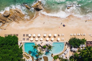 Açık havuzu ve güneş pansiyonları olan ilk hat plaj otelinin havadan görünüşü. Yaz tatillerinin kuş bakışı manzarası, turkuaz deniz suyu ve temiz kum kıyısındaki şemsiyeler.