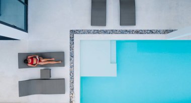 Havadan görünüşlü, kırmızı mayo giymiş kaygısız bir kadın turist lüks modern bir villada dinlenirken yaz tatilinin tadını çıkarıyordu. Kiralık evde dinlenen genç bir kadın.