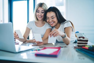 Neşeli çok ırklı kız arkadaşlar birbirlerine yaslanıyor ve çalışma odasındaki resimlere bakıp gülüyorlar. Birlikte vakit geçiriyorlar.