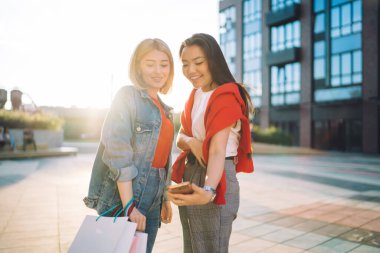 Arka sokaktaki alışveriş merkezinin yakınında dikilirken cep telefonuyla selfie çeken neşeli, çok ırklı genç bayan arkadaşlar.