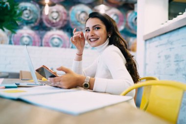 Başarılı bir bayan öğrenci, eğitim süresince cep telefonu uygulaması ile arıyor modern laptop teknolojisini öğreniyor, elinde akıllı telefon cihazıyla mutlu bir milenyum geçiriyor ve gülümsüyor.