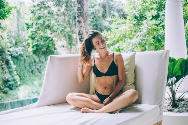 美しい笑顔幸せな健康フィットカジュアル若い女性で水着座って上の快適なソファで緑のスパテラス上の夏の日 — ストック写真