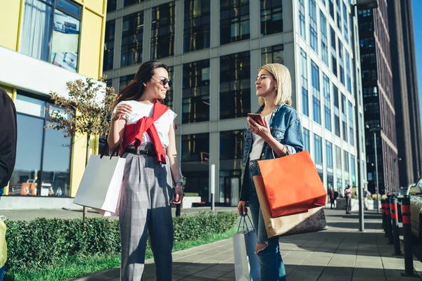 Zufriedene Trendige Freundinnen Die Mit Einkaufstüten Spazieren Gehen Während Sie — Stockfoto