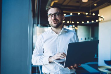 Yaratıcı, neşeli, sakallı iş adamı dizüstü bilgisayarda mesaj yazıyor. Akşamları ofiste beklenmedik haberler karşısında kameraya gülümsüyor.
