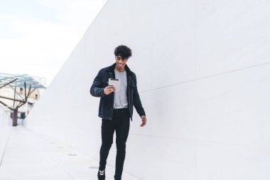 Modern stil gülümseyen genç esmer Afro-Amerikalı adam gün ışığında şehir caddesi tünelinde yürürken tablet üzerinde geziniyor.