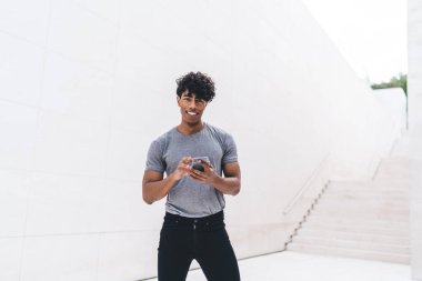 Elinde modern cep telefonu cihazı olan neşeli hippi adamın yarım boy portresi kameraya bakıyor ve gülümsüyor. Cihazlı bir adam tebligat yüklemek için dışarıda boş zaman harcıyor.