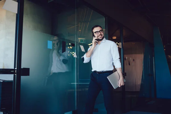 청록색 셔츠와 파란색 바지를 긍정적 유리문 반대로 사무실에서 전화로 말하는 — 스톡 사진