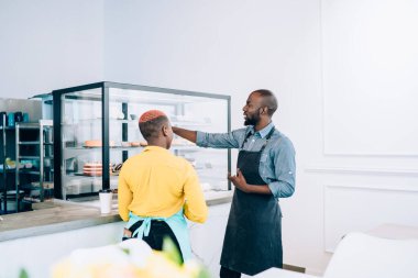 Afro-Amerikalı genç, modern kadın ve erkek birbirleriyle tartışıyor ve kafeteryadaki tatlılarla vitrine işaret ediyorlar.