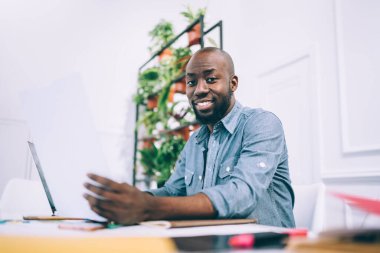 Belgelerle çalışan, dizüstü bilgisayarla sörf yapan, yaratıcı stüdyoda, saksıda çiçeklerle oturan, gülen Afro-Amerikan erkeklerinden.