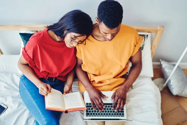 从上面看非洲裔美国女人看书 靠在黑人男朋友的肩上 一边用笔记本电脑 一边舒服地睡在一起 — 图库照片