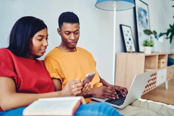 African American marriage using modern technology for shopping together discussing web discounts received in email, dark skinned husband and wife reading text publication connecting to home internet