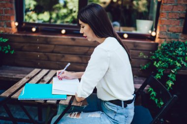 Çekici Latin öğrenci kafe terasında oturuyor ve üniversite kompozisyonu için bilgi yazıyor. Öğrenim sürecine odaklanmış, açık havada okuyan zeki bir öğrenci ders kitabına notlar yazıyor.