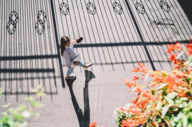 Üniversite kampüsüne giden eğitim ekipmanı ve akıllı telefon cihazıyla Latin kız öğrencilerin üst düzey görüntüsü. Şehir caddesinde cep telefonuyla yürüyen havalı giyinmiş serbest çalışan birinin havadan bakışı.