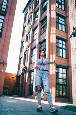 Modayı takip eden gözlüklü hippi kız portresi arka planda binalarla şehir caddesinde dikilip kameraya bakıyor.