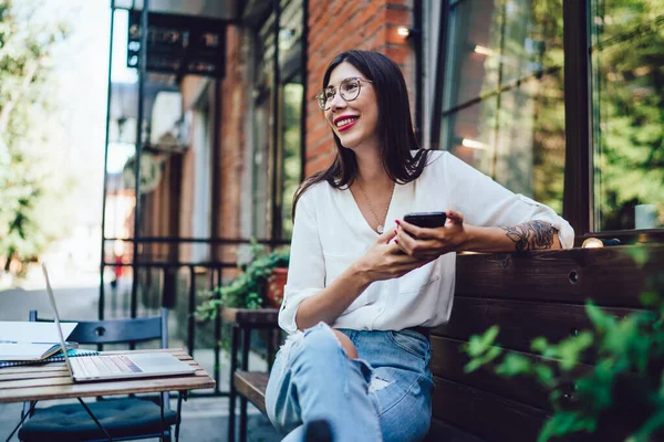 Neşeli, gülümseyen, beyaz tişörtlü, akıllı telefonuyla mesaj atan, şehir kafesindeki terasta oturan modern bir bayan. 