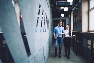 Zarif meslekdaşlar, modern ofiste iş tartışırken, koridorlarda dokümanlarla dolaşmaktan zevk alırlar.